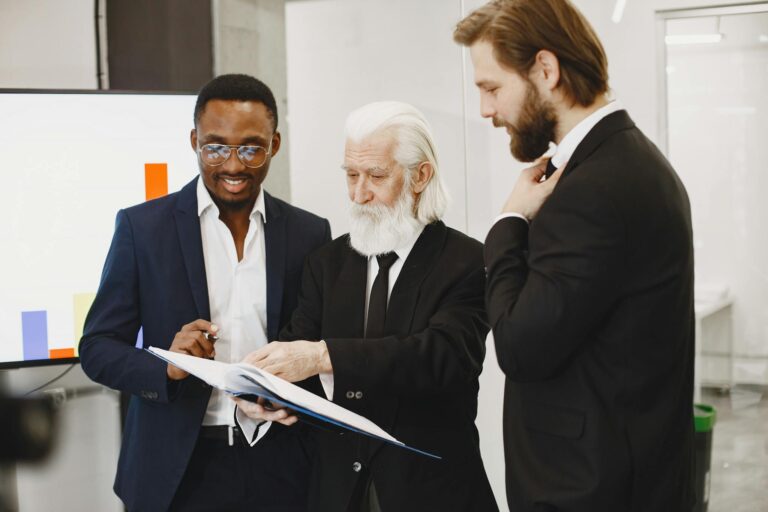 Three businessmen in suits reviewing documents in a modern office setting.